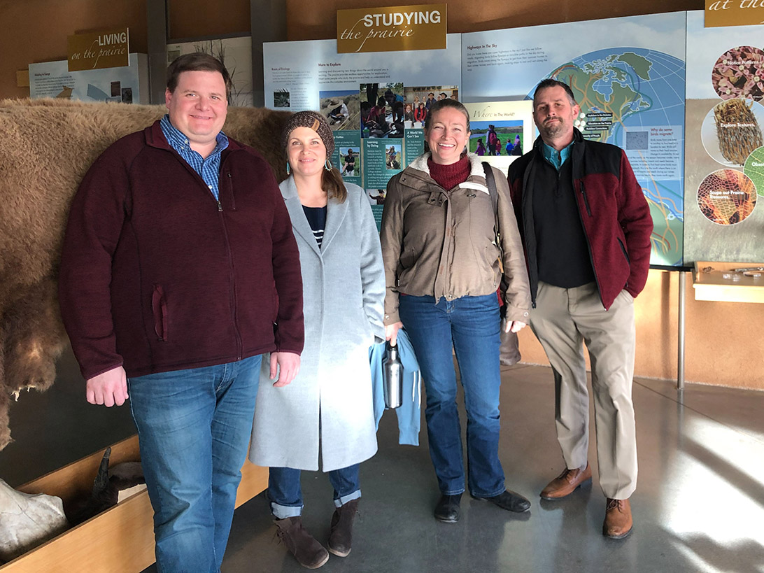 Four people stand and smile at the camera. Behind them are indoor exhibits and a taxidermy bison.